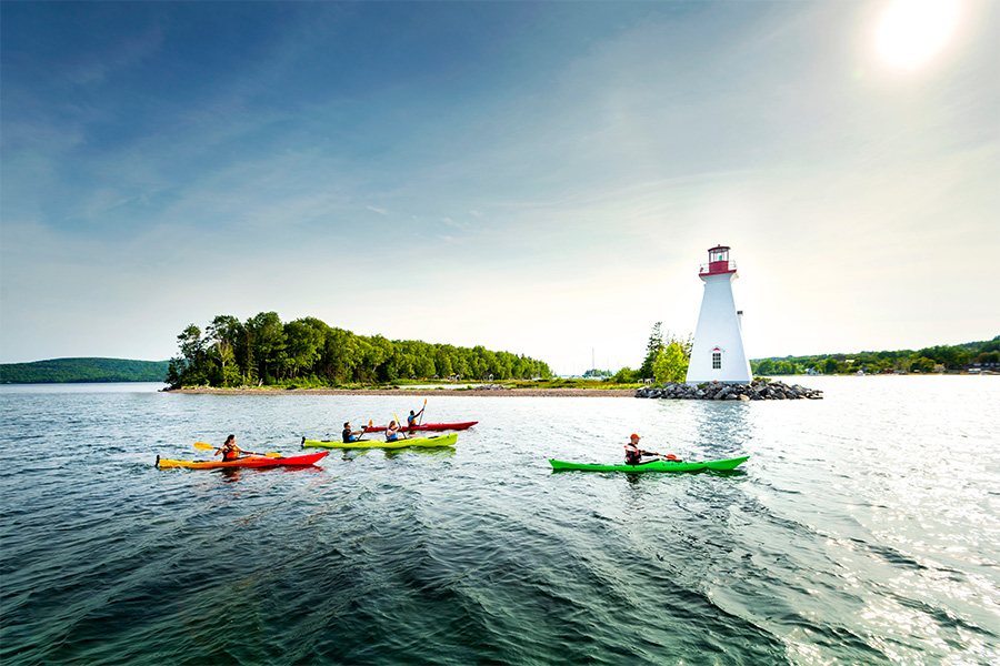 Kayakers passing a lighthouse in Baddeck.